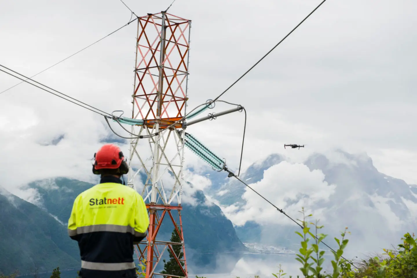 A Statnett technician inspecting a high-voltage power line tower in the Nordic mountains as part of the Nordic Market Management System (NMMS) project for aFRR and mFRR services